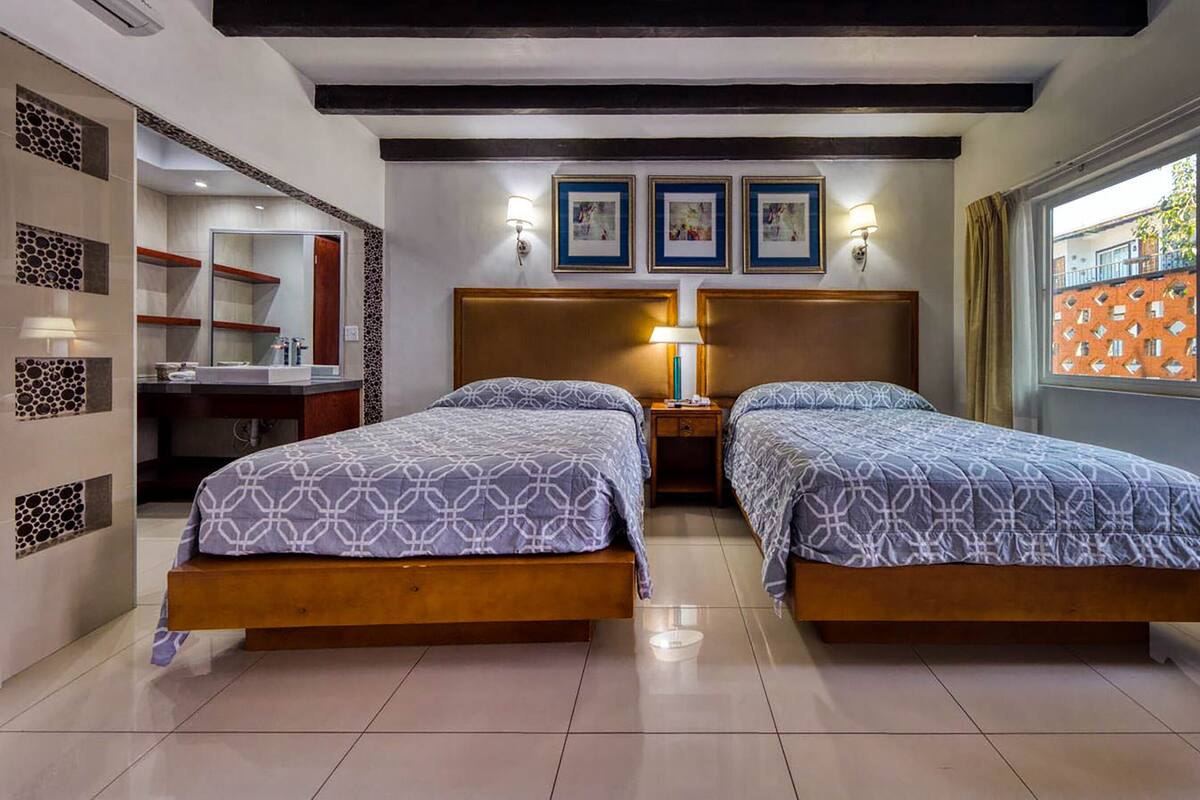Habitación de hotel con dos camas, baño y ventana con vistas.
