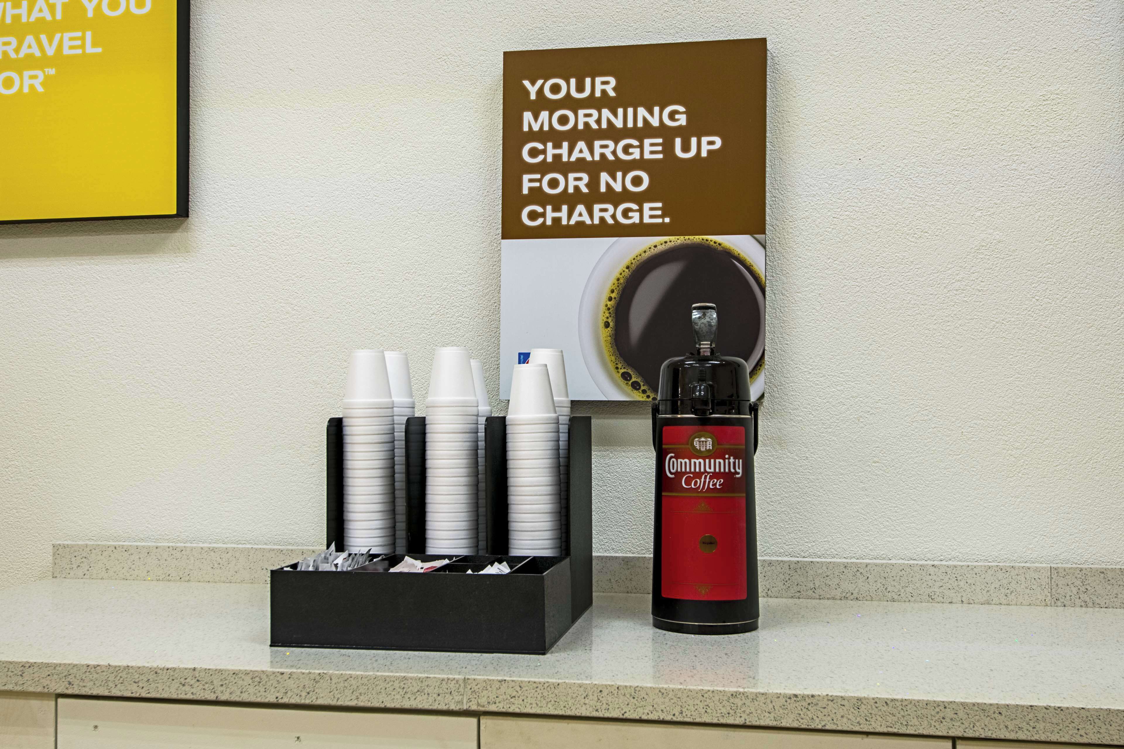 A coffee station with disposable cups, a coffee dispenser, and a sign advertising free morning coffee.