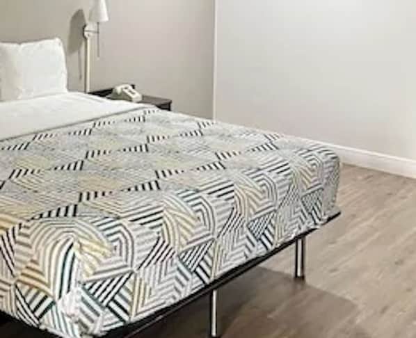 A bed with a patterned bedspread, a bedside table with a lamp, and a wooden floor. - Motel 6 Opelousas, LA (Opelousas)