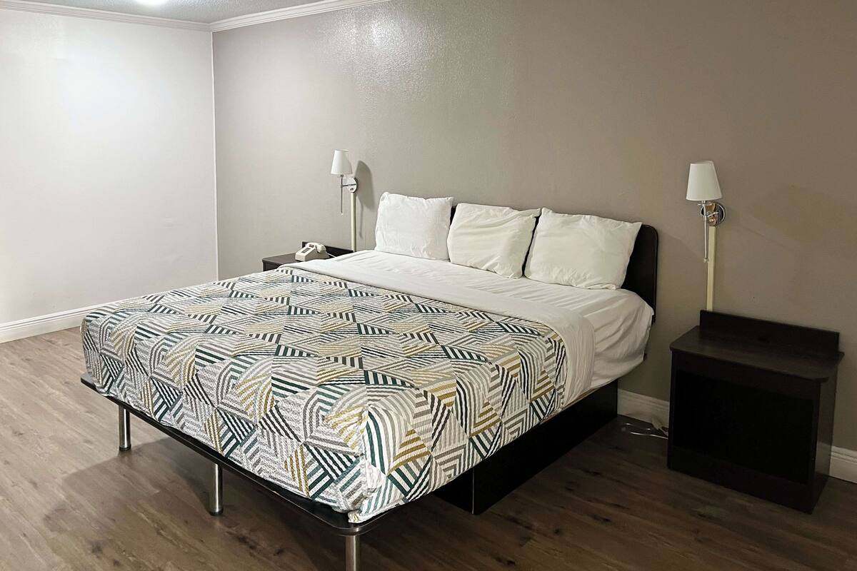 A neatly made bed with a patterned bedspread, two bedside lamps, and a nightstand with a phone.