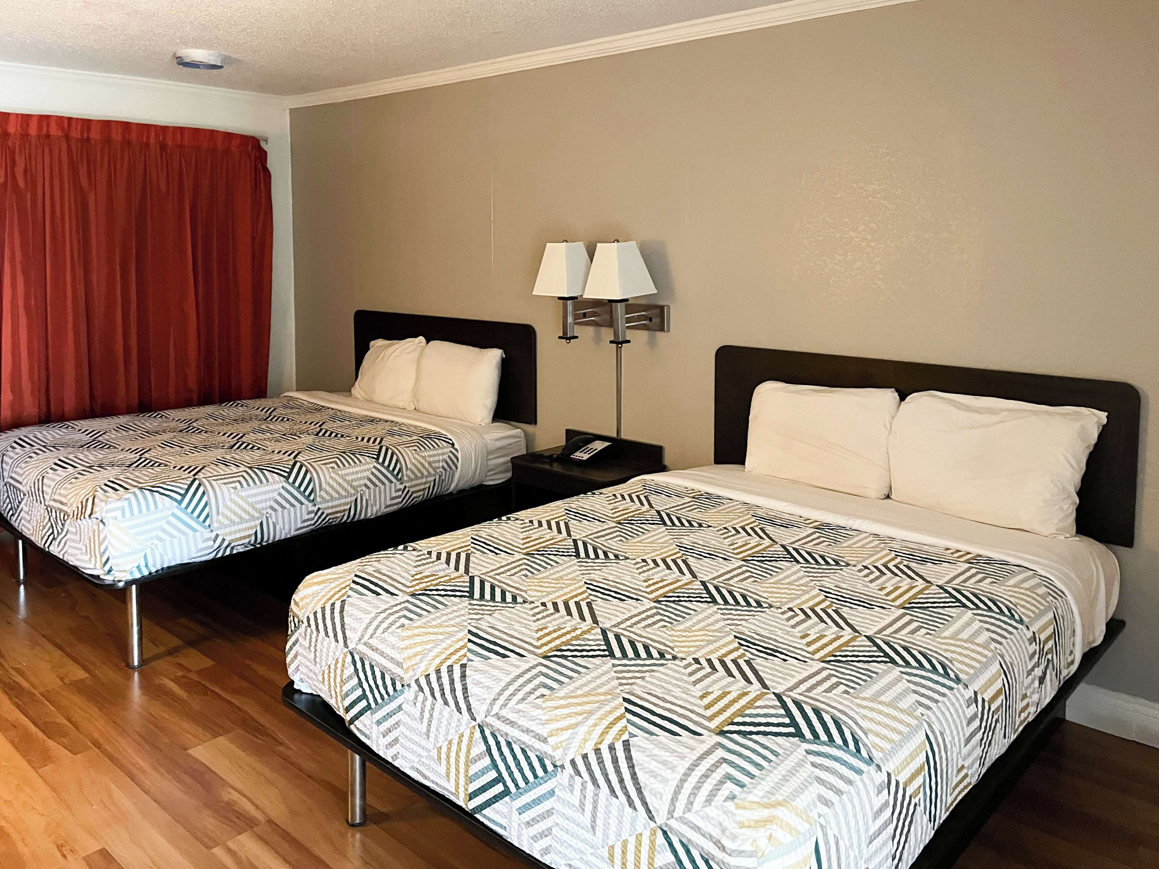 Two single beds with patterned bedding, a nightstand with a lamp, and a red curtain.