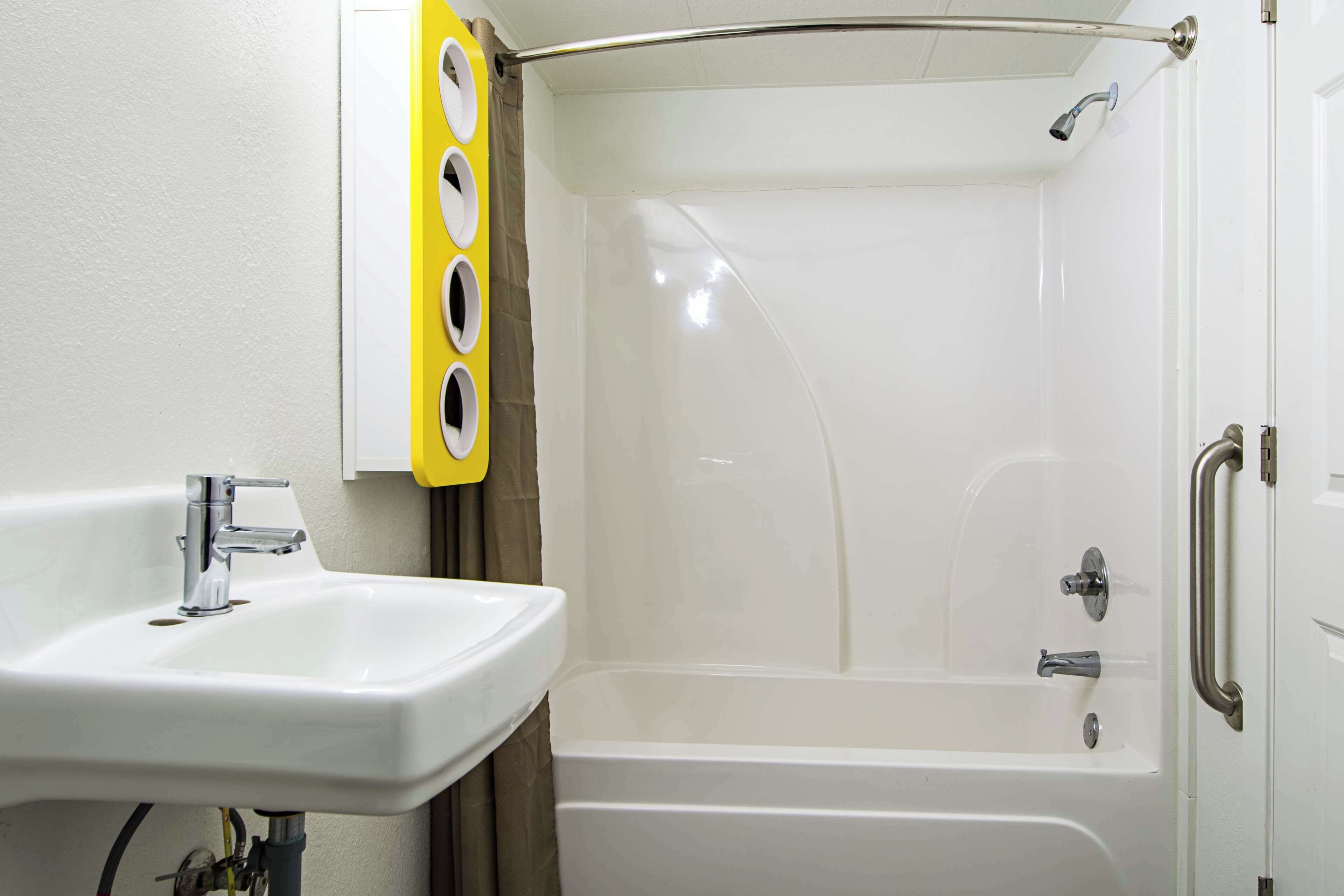 Un baño con un lavabo blanco, una ducha con puerta de cristal y un perchero amarillo.