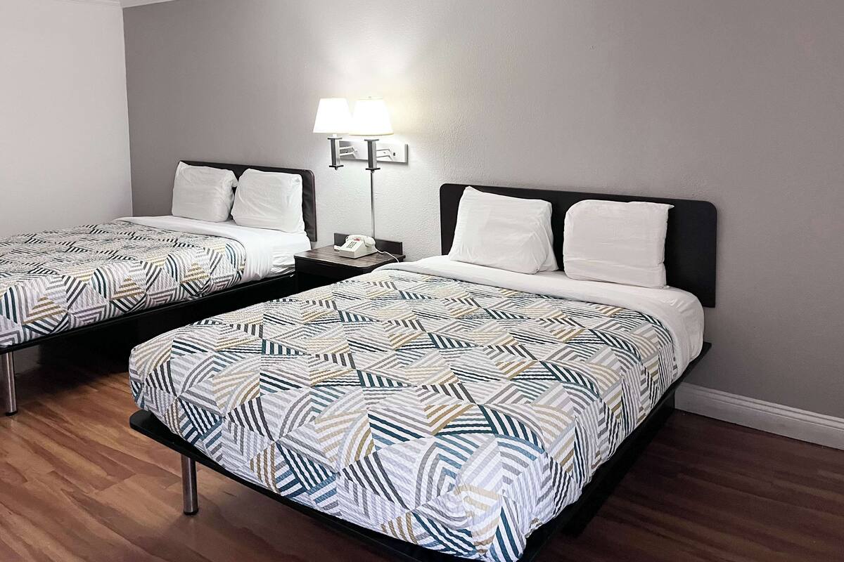 A hotel room with two beds, each with a patterned bedspread, a bedside table with a lamp, and a phone.