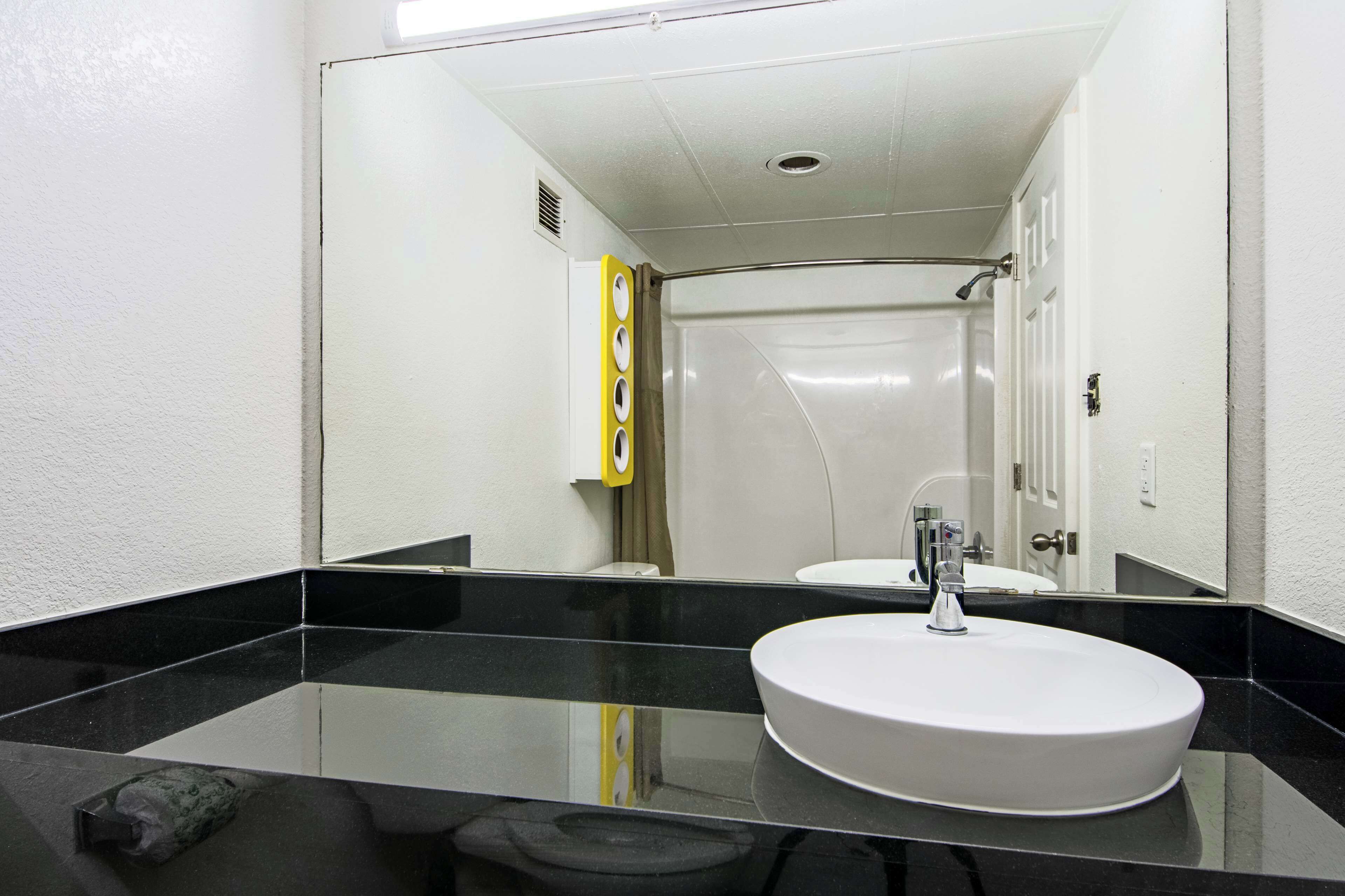 A bathroom with a black countertop, a white sink, and a mirror reflecting a shower area.