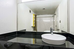 A bathroom with a black countertop, a white sink, and a mirror reflecting a shower area. - Motel 6 Opelousas, LA (Opelousas)