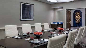 A conference room with a long table, white chairs, and a blue decorative piece on the wall.