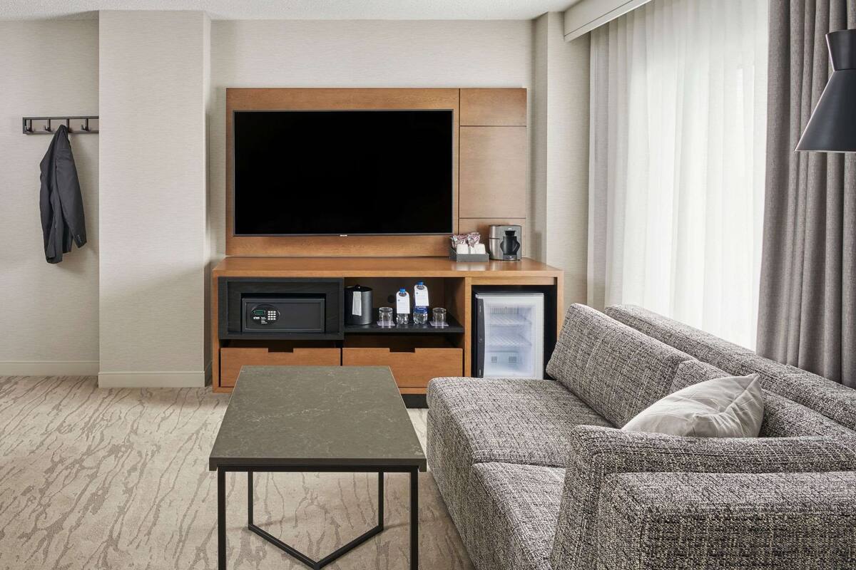 Une chambre d’hôtel moderne équipée d’une télévision à écran plat, d’une machine à café, d’un mini-réfrigérateur et d’un canapé.