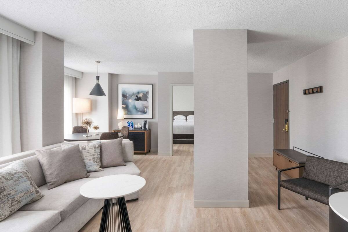 Une chambre d’hôtel moderne, équipée d’un canapé, d’une petite table ronde, d’un bureau avec une chaise, d’un lit et d’un grand miroir.