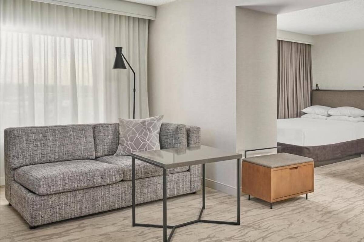 Une chambre d’hôtel comprenant un canapé, une petite table, une table d’appoint en bois, un lit et une table de chevet.