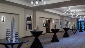 Un pasillo de hotel con varias mesas y jarrones decorativos, que incluye una lámpara de araña moderna y obras de arte enmarcadas en las paredes.