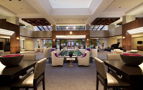 A spacious lobby with a central seating area, a piano, and a large window overlooking a garden.