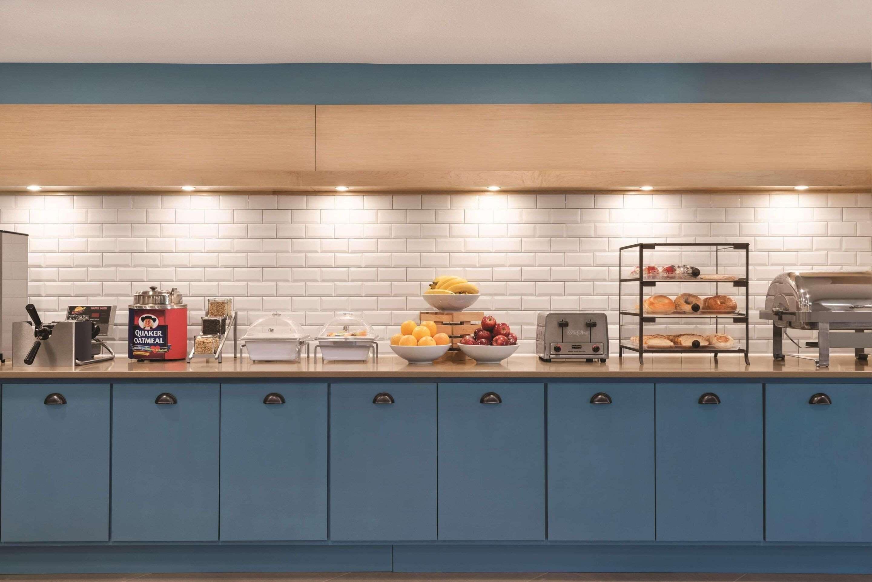 Una cocina con armarios azules, salpicadero de azulejos blancos y diversos alimentos para el desayuno sobre la encimera.