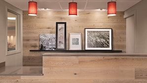 A reception desk with a wooden finish, three pendant lights, and framed artwork on the wall. - Country Inn & Suites by Radisson, Northfield, MN (Northfield)