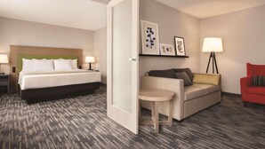 A hotel room with a bed, a sofa, a small table, a red armchair, and a lamp. - Country Inn & Suites by Radisson, Northfield, MN (Northfield)