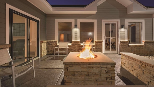 An outdoor patio with a stone fire pit, seating, and a covered area with windows. - Country Inn & Suites by Radisson, Northfield, MN (Northfield)