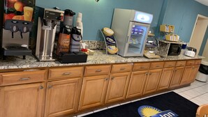 A hotel kitchen with a coffee station, refrigerator, microwave, toaster, and a Days Inn logo on the floor. - Days Inn by Wyndham Cartersville (Cartersville)