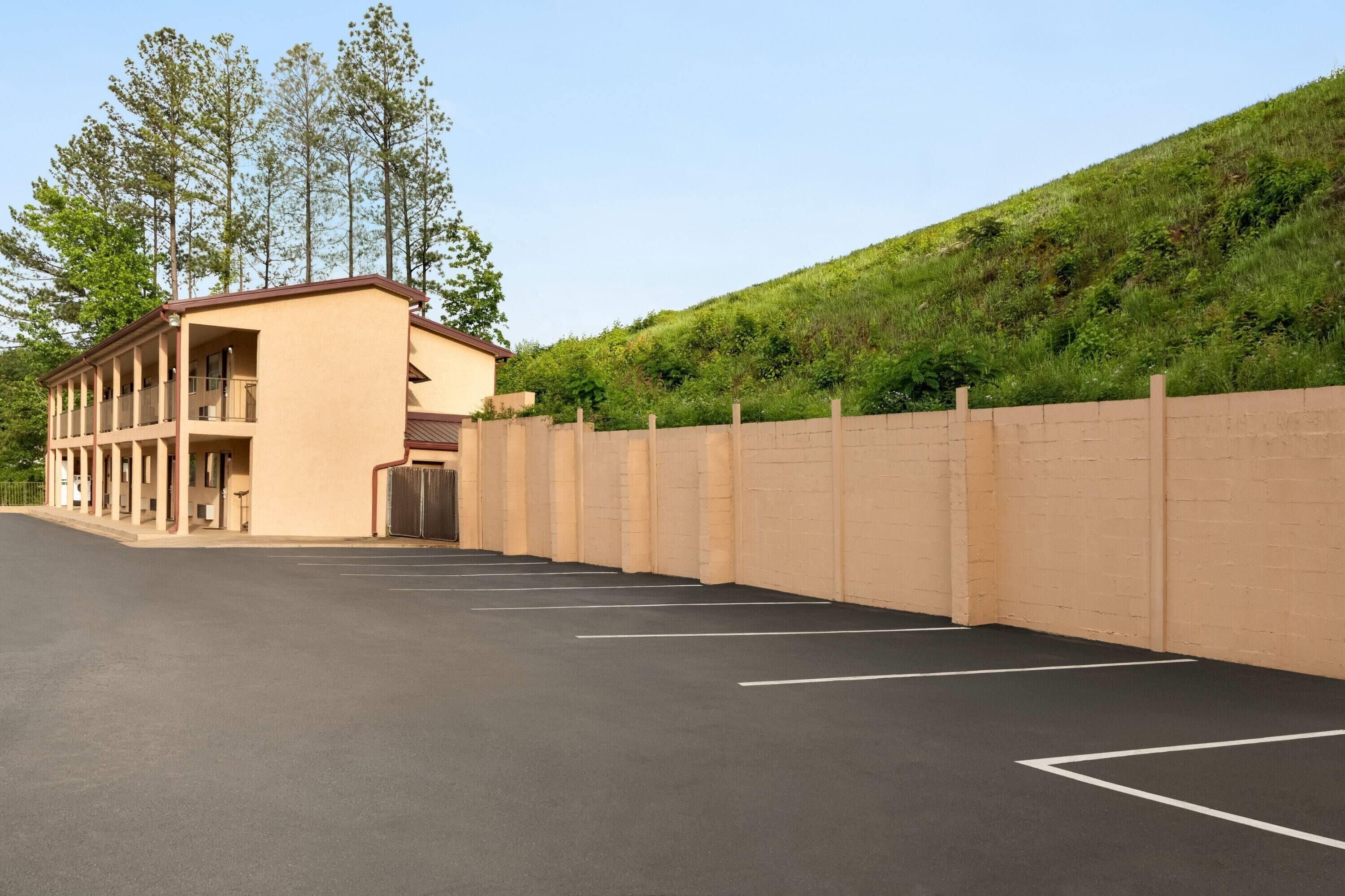 A building with a parking lot, a covered area with columns, and a hillside with trees.