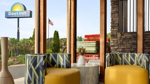 A Days Inn by Wyndham lobby with two yellow cushioned seating areas, a stone wall, and a view of the parking area. - Days Inn by Wyndham Cartersville (Cartersville)