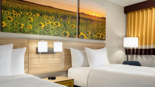 A hotel room with two beds, a large sunflower painting on the wall, a nightstand, and a lamp. - Days Inn by Wyndham Cartersville (Cartersville)