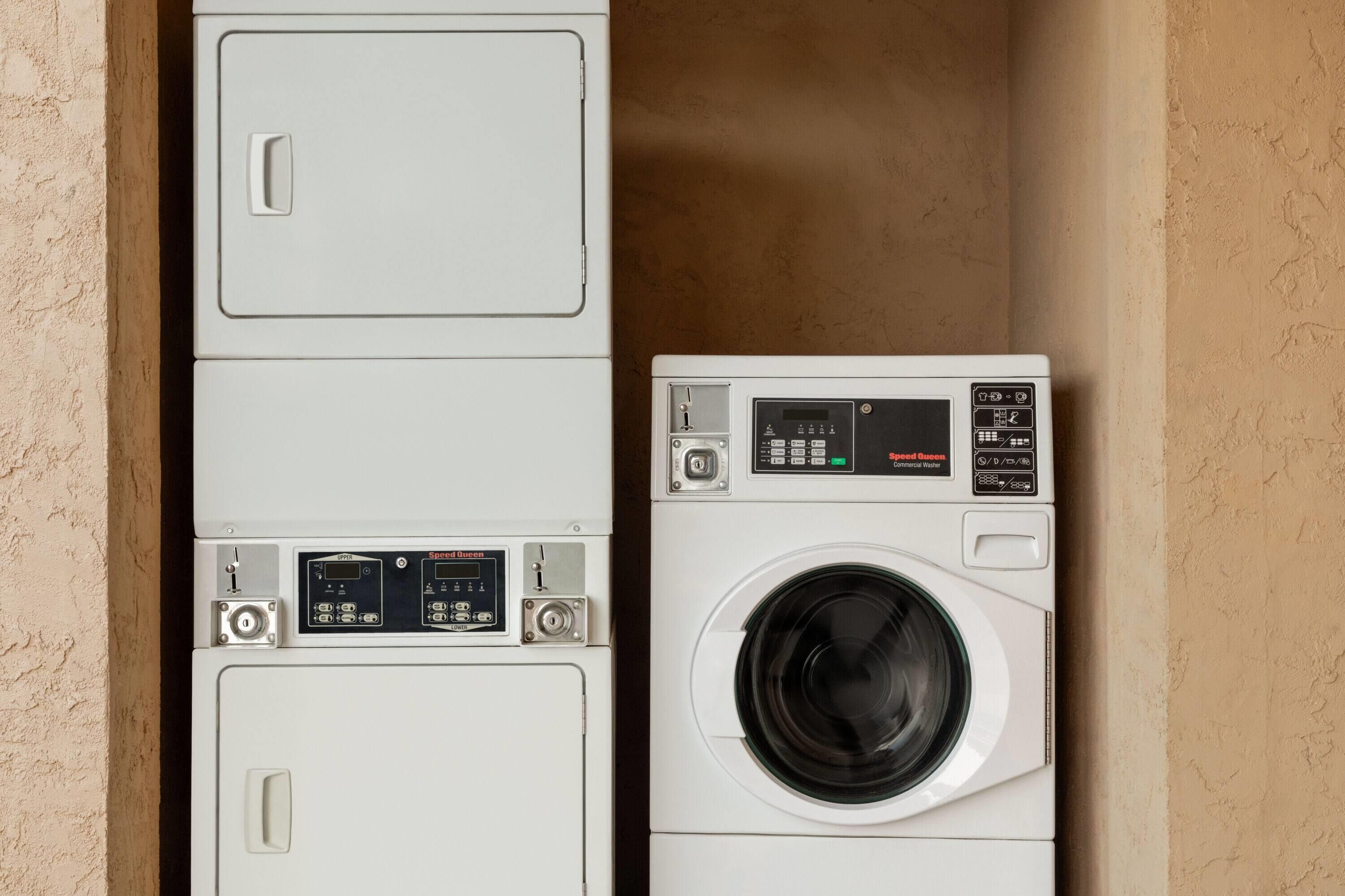 Un cuarto de lavandería con lavadoras y secadoras apiladas, incluyendo una lavadora de carga frontal con panel de control digital.