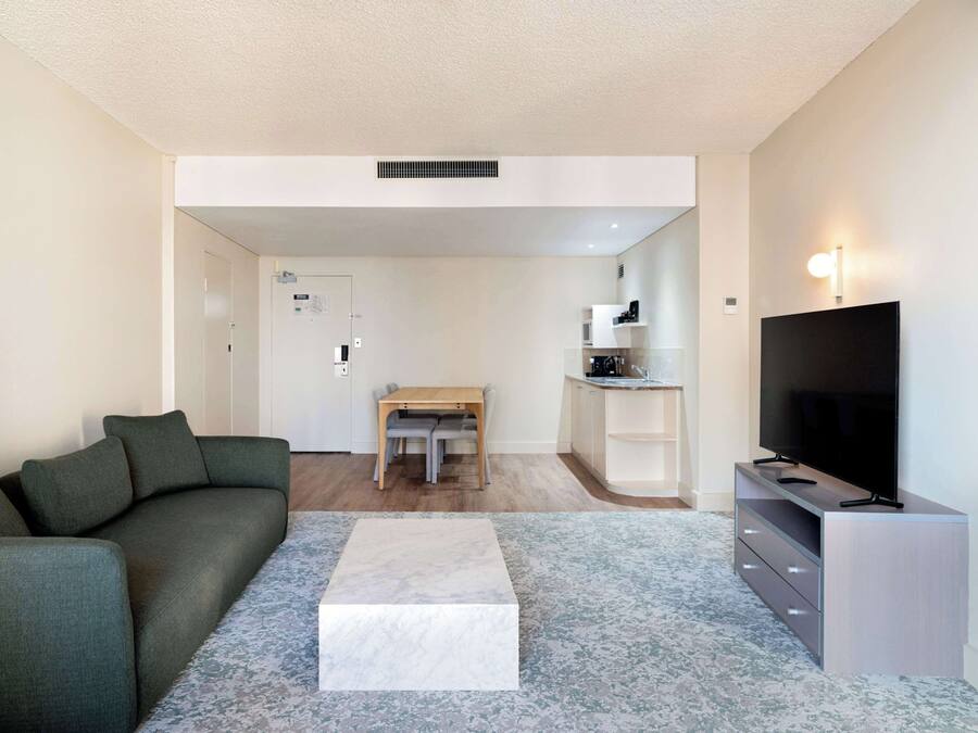 A modern living room with a sofa, a coffee table, a TV stand, and a dining area with a table and chairs.