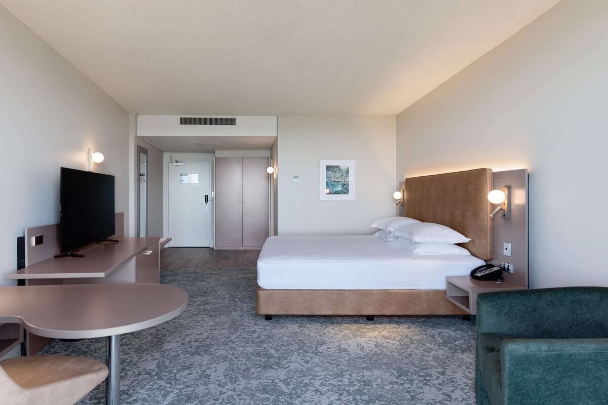 Una habitación de hotel con cama, escritorio, silla, televisión y mesita de noche con lámpara.