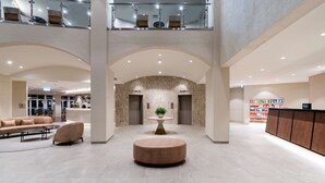 A spacious lobby with a central round seating area, a reception desk, and a high ceiling with a glass railing.