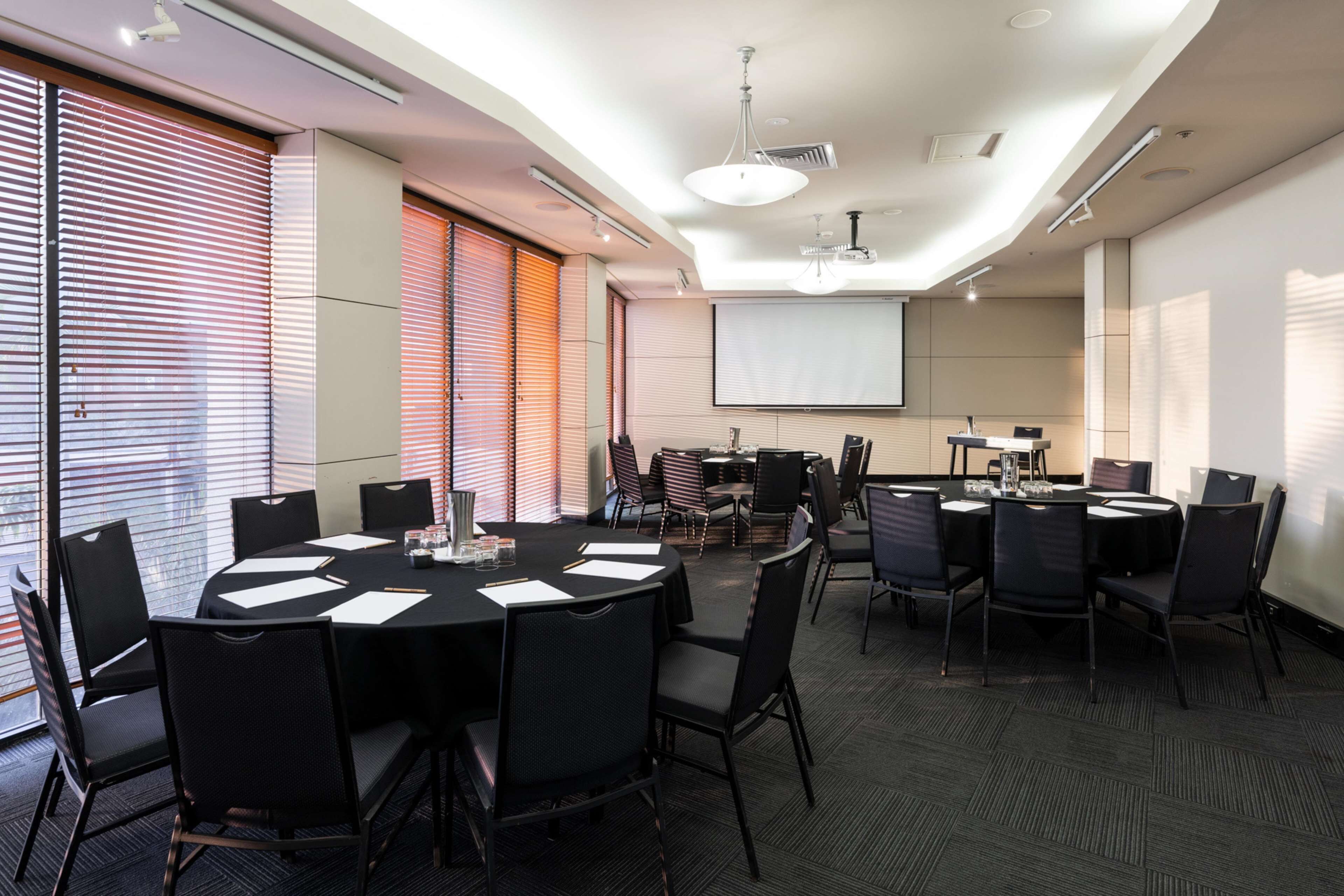 A conference room with a large screen, multiple tables, and chairs.