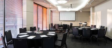 A conference room with a large screen, multiple tables, and chairs.
