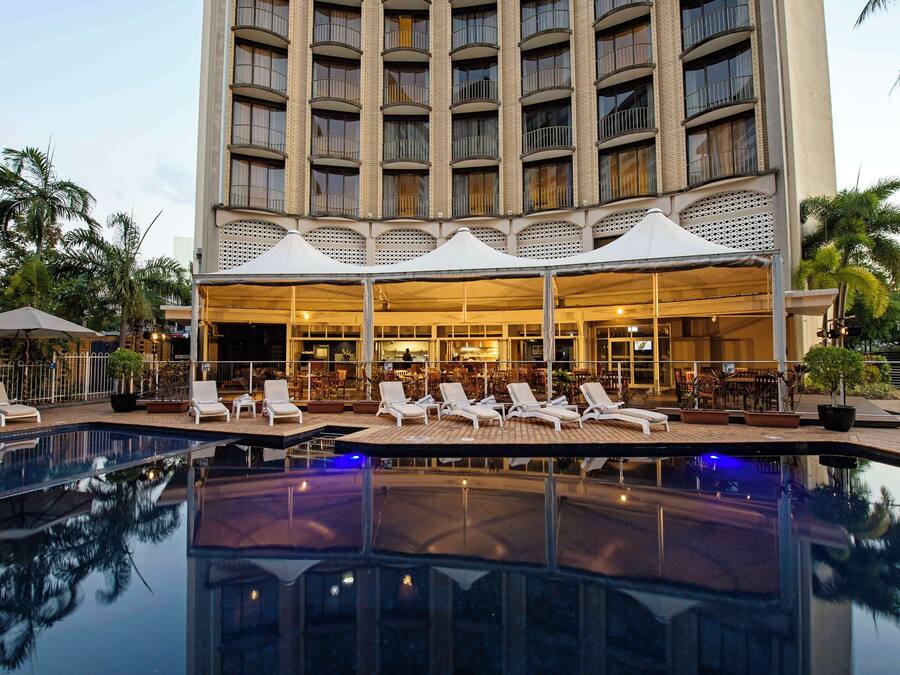 A hotel with a pool, lounge chairs, and a bar area.