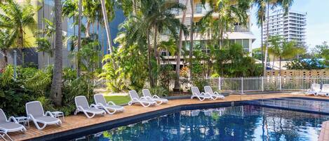 Una piscina con sillas de descanso, rodeada de palmeras y edificios modernos.