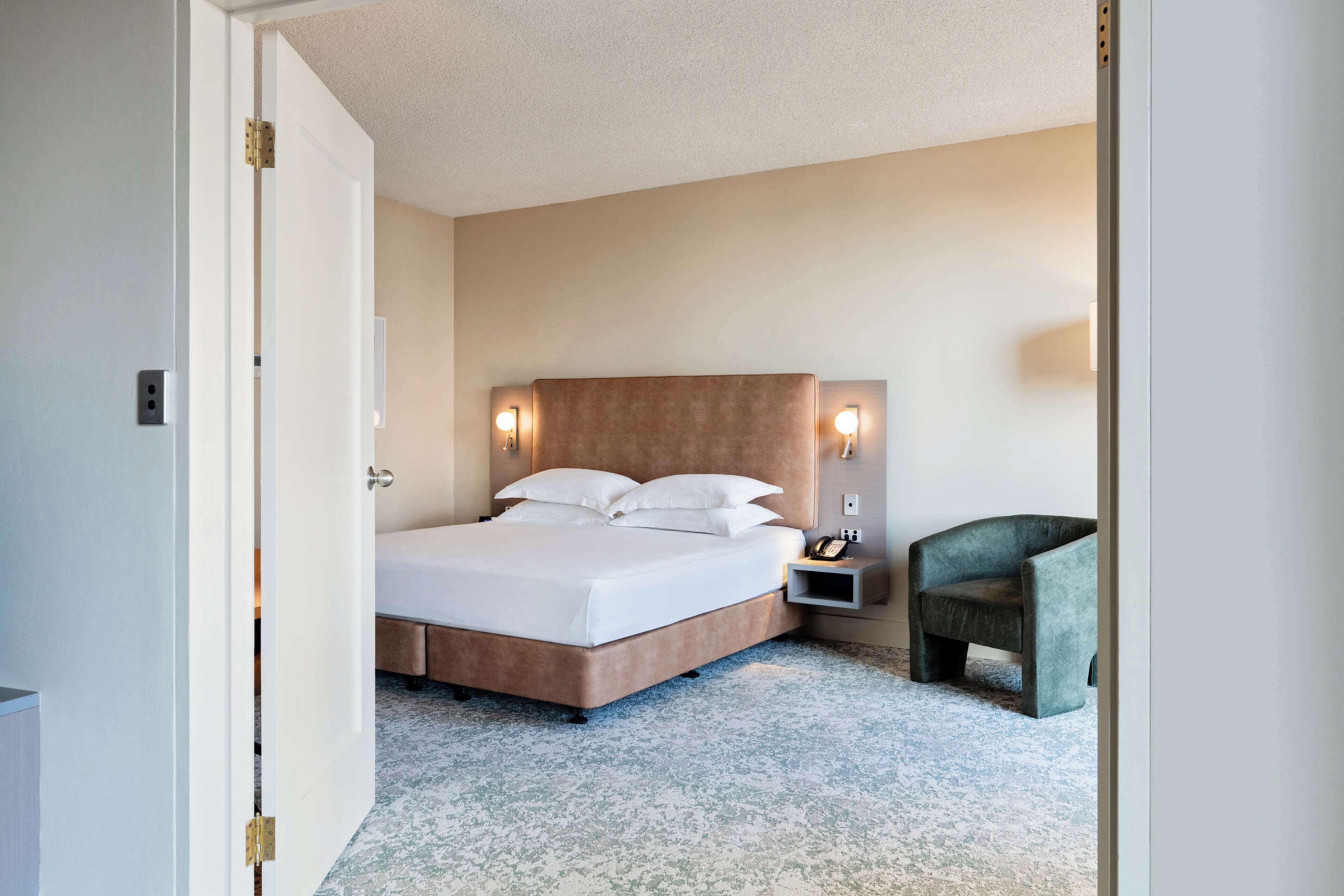 Une chambre d’hôtel comprenant un lit, une table de chevet, une chaise et une lampe fixée au mur.
