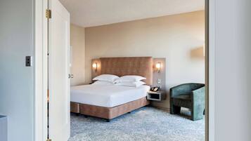 Una habitación de hotel con cama, mesita de noche, silla y una lámpara de pared.