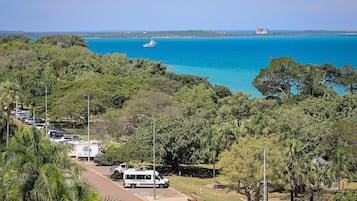 Vista costera con puerto deportivo, vehículos estacionados y abundante vegetación.