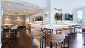 A modern bar area with high stools and a central round table, featuring a bar counter and seating area with a view of the outdoors.