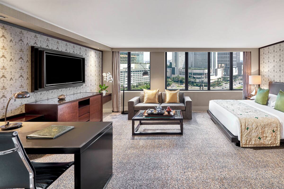Habitación de hotel con una cama grande, un sofá, un televisor, un escritorio y vistas a la ciudad.