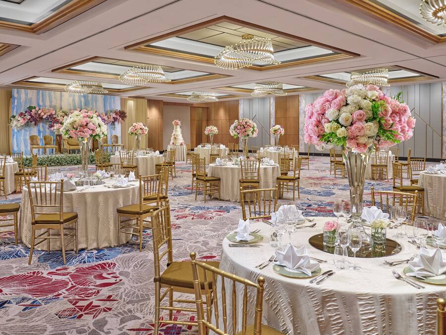 A banquet hall with round tables set for dining, gold chairs, and large floral centerpieces.