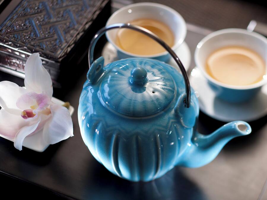 Um bule azul com tampa e cabo, duas xícaras de café e uma orquídea branca.