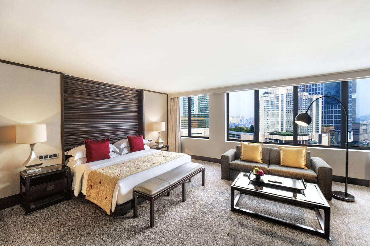 Habitación de hotel con una cama grande, un sofá, una mesa de centro y vistas a la ciudad.