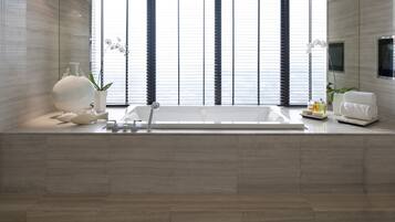 A modern bathroom with a large bathtub, a window with blinds, a white orchid plant, and a white chair.