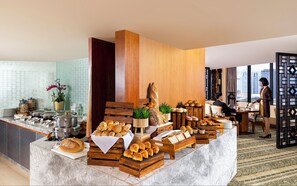 A breakfast buffet with various breads and pastries, a coffee station, and a view of the city through large windows. - Mandarin Oriental, Jakarta (Jakarta)