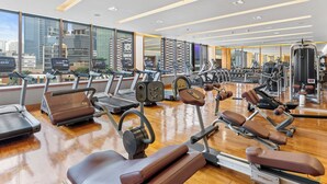 Un gimnasio moderno con cintas de correr, elípticas y equipos de pesas. Amplios ventanales ofrecen vistas de un paisaje urbano.