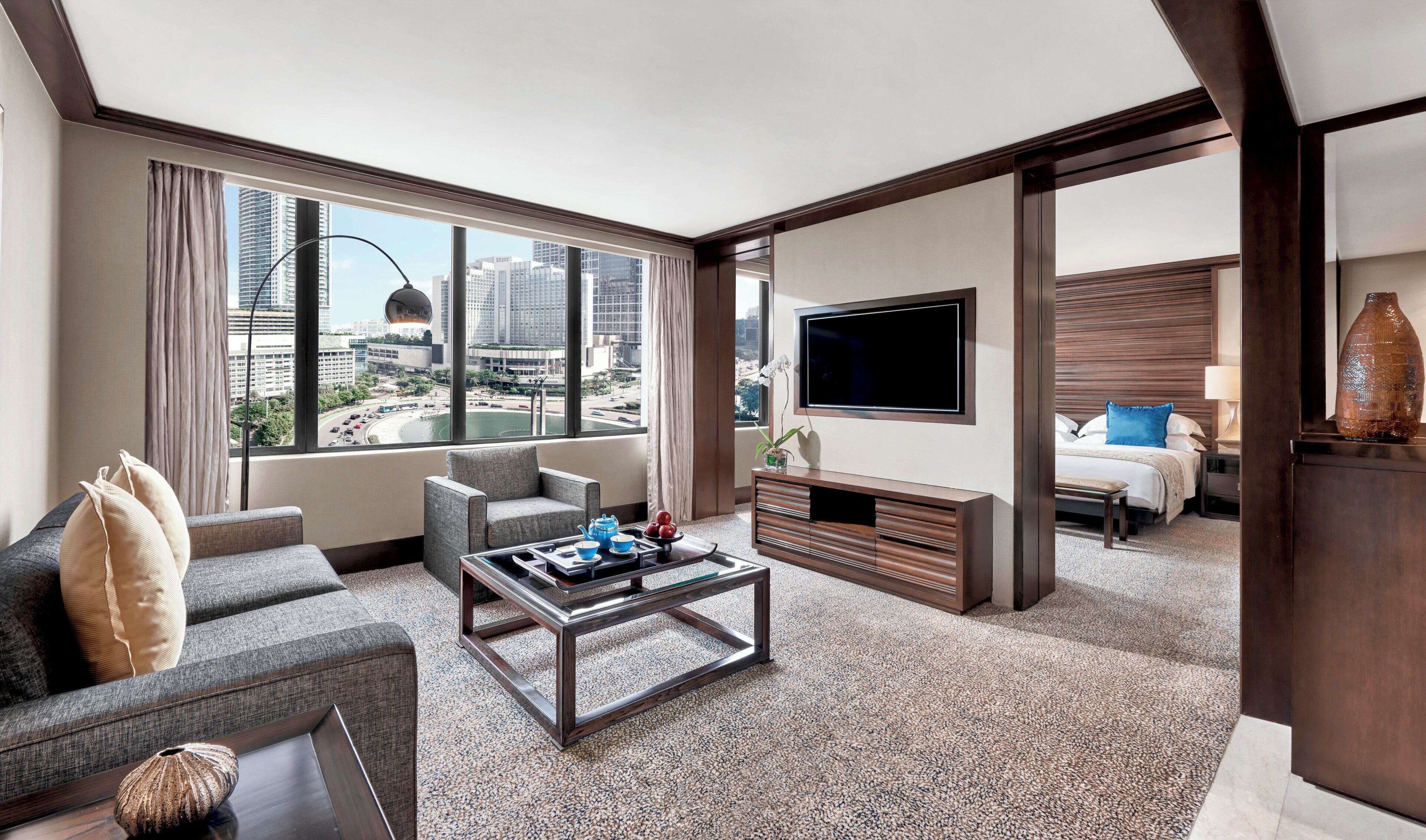 Habitación de hotel con vista a la ciudad, televisión de pantalla plana, sofá, mesita de centro y cama con mesita de noche.