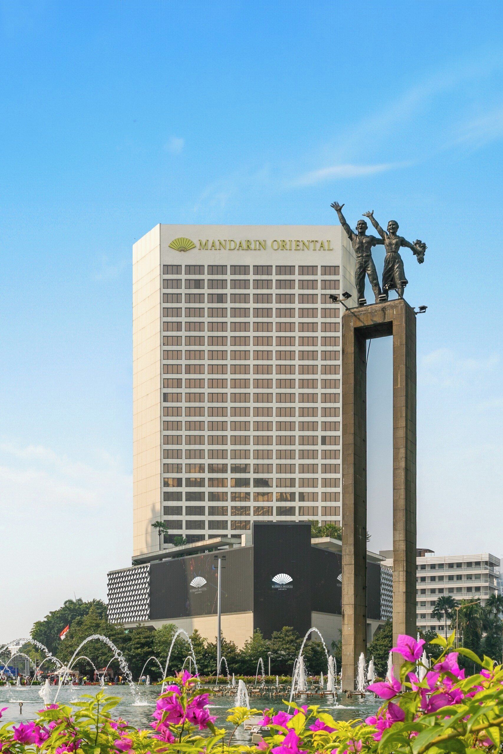 A tall building with a sign reading "MANDARIN ORIENTAL" and a statue of two figures on top.