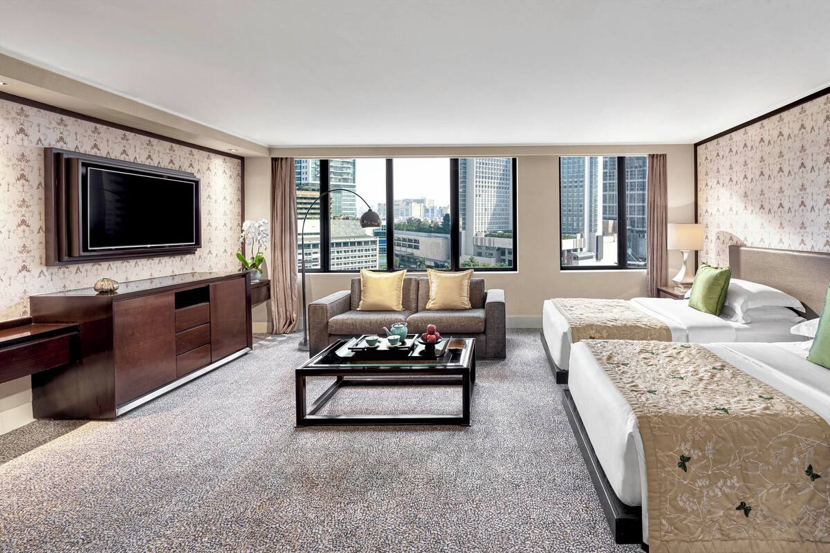 Habitación de hotel con una televisión grande, un sofá, una cama y vistas a la ciudad.