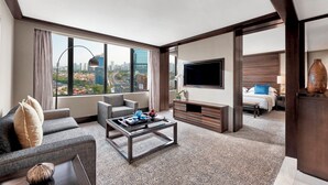 Una habitación de hotel moderna con vista a la ciudad, un televisor de pantalla plana, un sofá, una mesa de centro y una cama con mesita de noche.