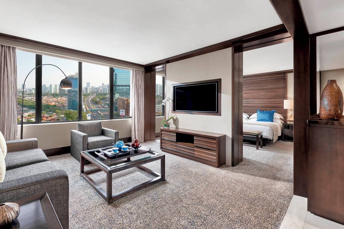 Una habitación de hotel moderna con vista a la ciudad, un televisor de pantalla plana, un sofá, una mesa de centro y una cama con mesita de noche.