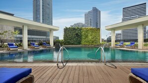 Una piscina en la azotea con agua azul cristalina, rodeada de sillones de descanso y una terraza de madera.