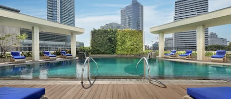 Una piscina en la azotea con agua azul cristalina, rodeada de sillones de descanso y una terraza de madera.
