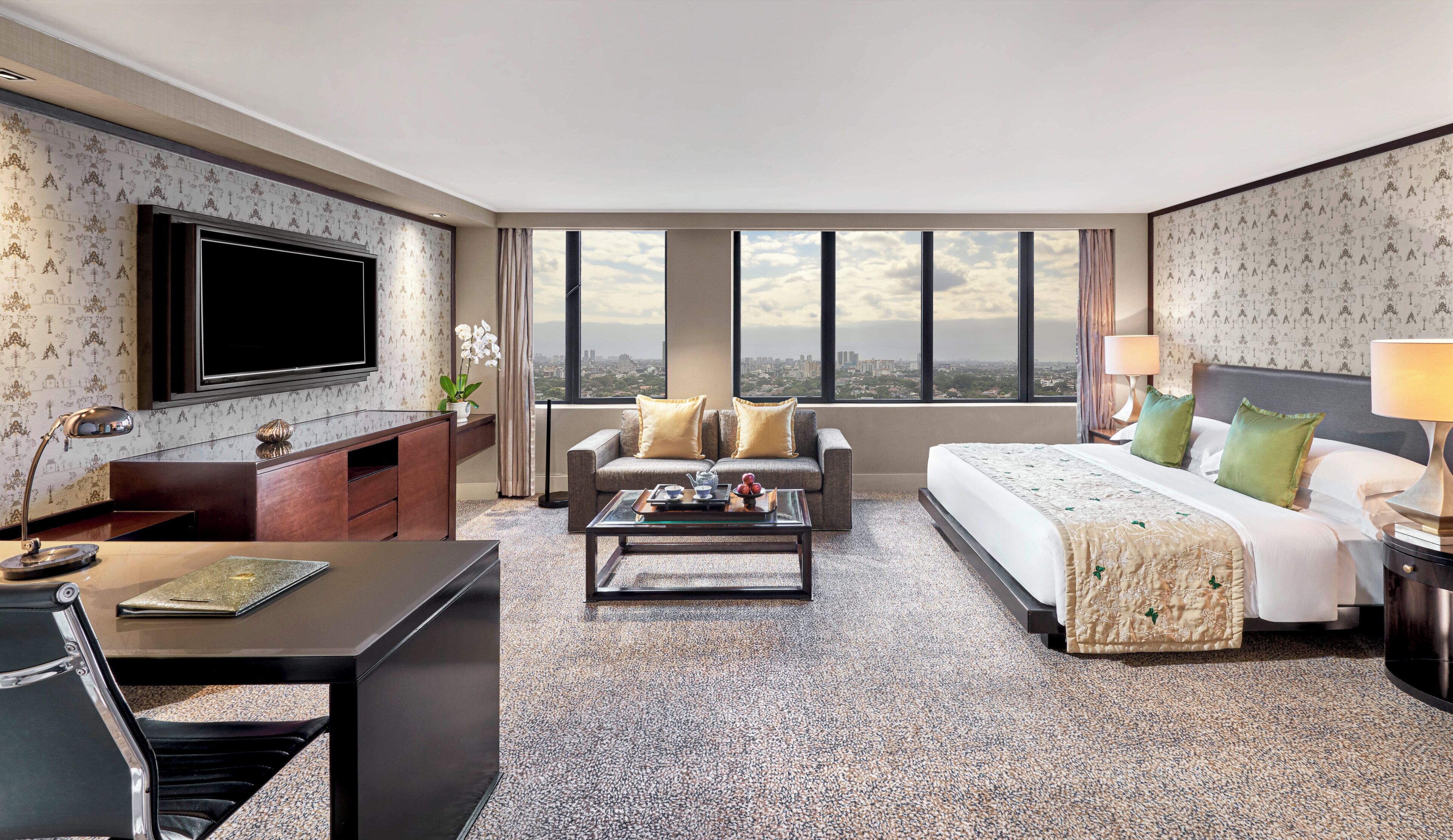 A hotel room with a large bed, a sofa, a TV, a desk, and a view of the city.